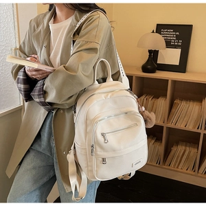 White faux leather backpack detail showing multi-zipper layers and side plush pom-pom