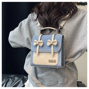 Detail of blue denim and beige leather backpack featuring two bows and handle
