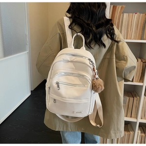 Detail of white litchi pattern leather backpack with plush pendant in library setting