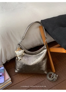 Macro detail of silver pleated underarm bag with plush doll charm and long strap