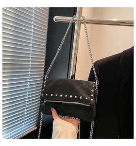 Close-up of matte black suede texture with silver metal studs and chain strap