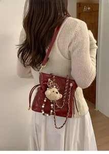 Detail of red quilted bucket bag with plush bear charm and elegant pearl strap
