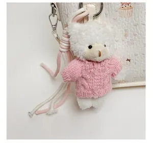 Detail of cute white plush bear charm with pink knitted sweater on leather tote bag