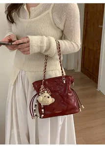 Detail of dark red quilted chain bucket bag featuring a cute plush bear charm accessory