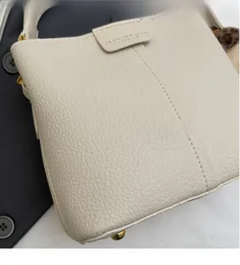 Dettaglio ravvicinato della borsa a secchiello beige con pelle a grana e logo inciso