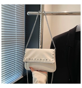 Close-up of white shoulder bag featuring silver rivets and metallic chain strap detail