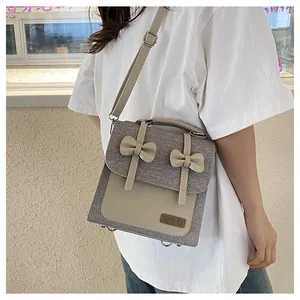 Detail of gray canvas crossbody bag with beige bows and adjustable leather shoulder strap