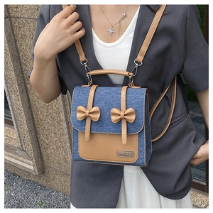 Close-up of blue denim backpack with brown leather bows and metal bear logo detail