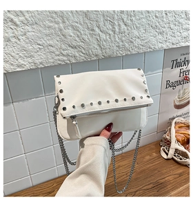 Detail of cream leather crossbody bag featuring silver stud rivets and a sleek metal chain