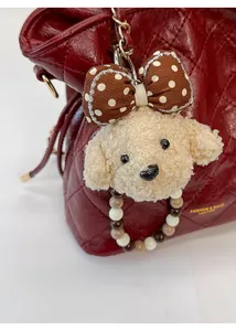Close-up of a plush puppy charm with beaded strap on a red quilted shoulder bag