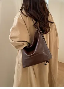 Detail of a large dark brown faux leather Hobo bag worn with a beige trench coat