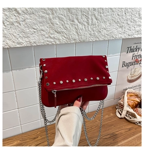 Detail of red suede crossbody bag featuring silver metal rivets and a stylish chain strap