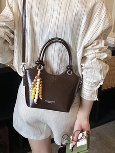 Deep brown glossy bucket bag with dual handles and beaded charm for women