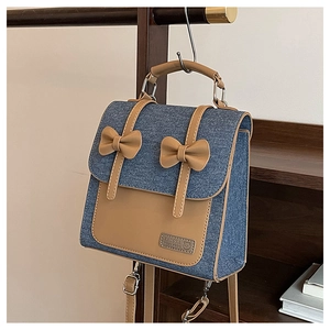 Detail of denim and leather bag with ribbon bows and KAUSNA logo on wooden stand
