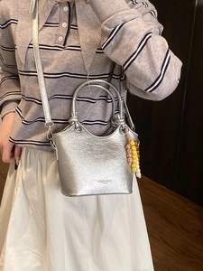 Metallic silver bucket bag with top handles and beaded charm shown on model