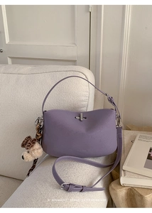 Detail of purple leather handbag with metal lock and cute plush dog charm on sofa