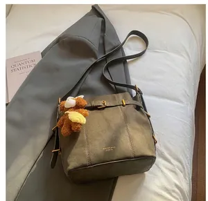 Detail der graubraunen Wildleder-Beuteltasche mit Lederriemen und braunem Bären-Anhänger