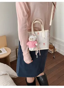 Detail of cute cream tote bag with cartoon print, teddy bear charm, and shoulder strap