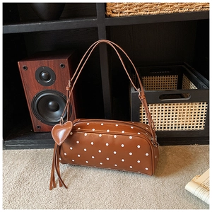 Detailed close-up of brown polka dot cylinder bag with heart charm and fringe tassel