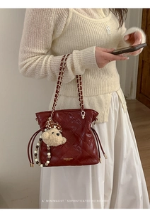 Detail of burgundy quilted bucket bag with gold chain strap and teddy bear charm