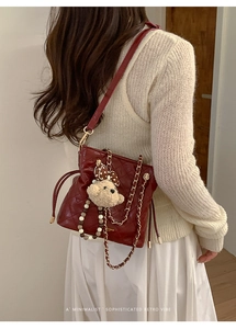 Detail of dark red quilted bucket bag with gold chain and bear charm on cream outfit