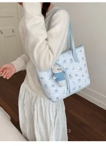 Detail of light blue printed tote bag featuring cute cartoon patterns and plush bear charm