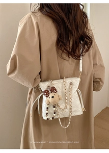 Detail of white quilted crossbody bag with gold chain and plush bear charm