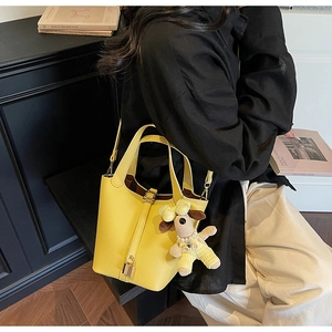 Close-up of a yellow pebbled leather bucket bag with dog charm and shoulder strap