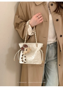 Detail of white quilted bucket bag with gold chain strap and cute bear charm pendant