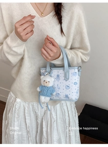 Detail of blue cartoon cat printed tote bag with a white plush bear keychain pendant
