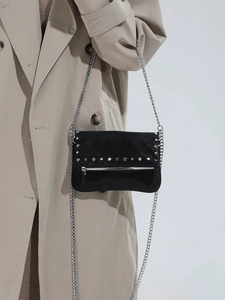 Fashionable black studded crossbody bag with silver chain strap shown on beige trench coat