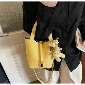 Detail of yellow lychee leather bucket bag with cute plush dog charm and gold lock buckle