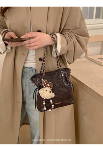 Close-up of dark brown quilted shoulder bag with chain strap and teddy bear charm