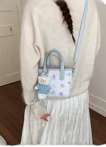 Detail of light blue tote bag featuring cute cartoon rabbit prints and a plush bear charm