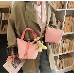 Detailed shot of pink lychee leather bucket bag set with a dog plush charm on a shelf