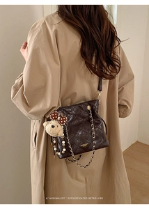 Detail of dark brown quilted leather bucket bag with gold chain and plush bear charm