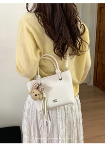 Detail of white PU tote bag with bear charm pendant and crossbody strap on model