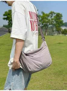Outdoor shot of a greyish purple nylon crossbody dumpling bag with adjustable strap