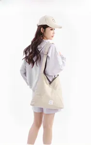 Borsa tote beige in nylon con tracolla regolabile indossata da modella in stile casual