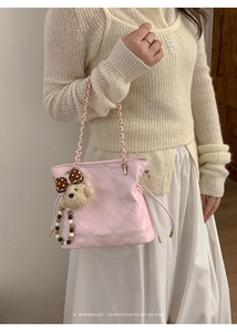 Pink quilted bucket bag detail with plush bear charm and chain handle shown on model