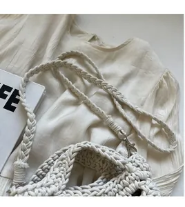 Detail of wide woven shoulder strap connected with metal buckle on a beige crochet bag