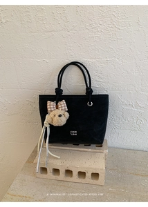 Detail view of black vintage bucket bag featuring a plush bear charm and rope handles