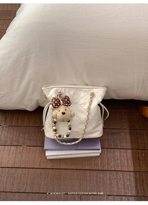 Detailed view of white quilted bucket bag with gold chain and cute plush bear charm