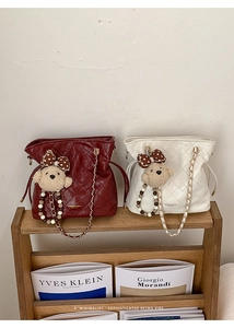 Close-up of quilted bucket bag featuring plush bear charm and golden chain strap detail