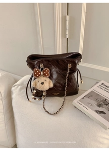 Macro detail of dark brown quilted leather bucket bag with gold chain and bear charm
