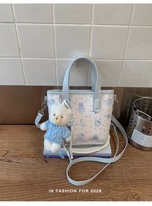 Detail of light blue cartoon tote bag with plush bear charm on white wooden background