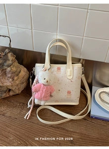 Close-up of cute cartoon cat tote bag with a plush bear charm on a vintage wooden desk