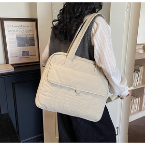 Dettaglio di una grande borsa tote trapuntata beige indossata da una modella in uno studio