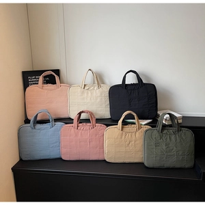 Rangée de sacs cabas matelassés en sept couleurs pastel exposés sur un podium noir