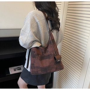 Detail of a brown Hobo bag featuring a geometric block pattern and wide leather shoulder strap
